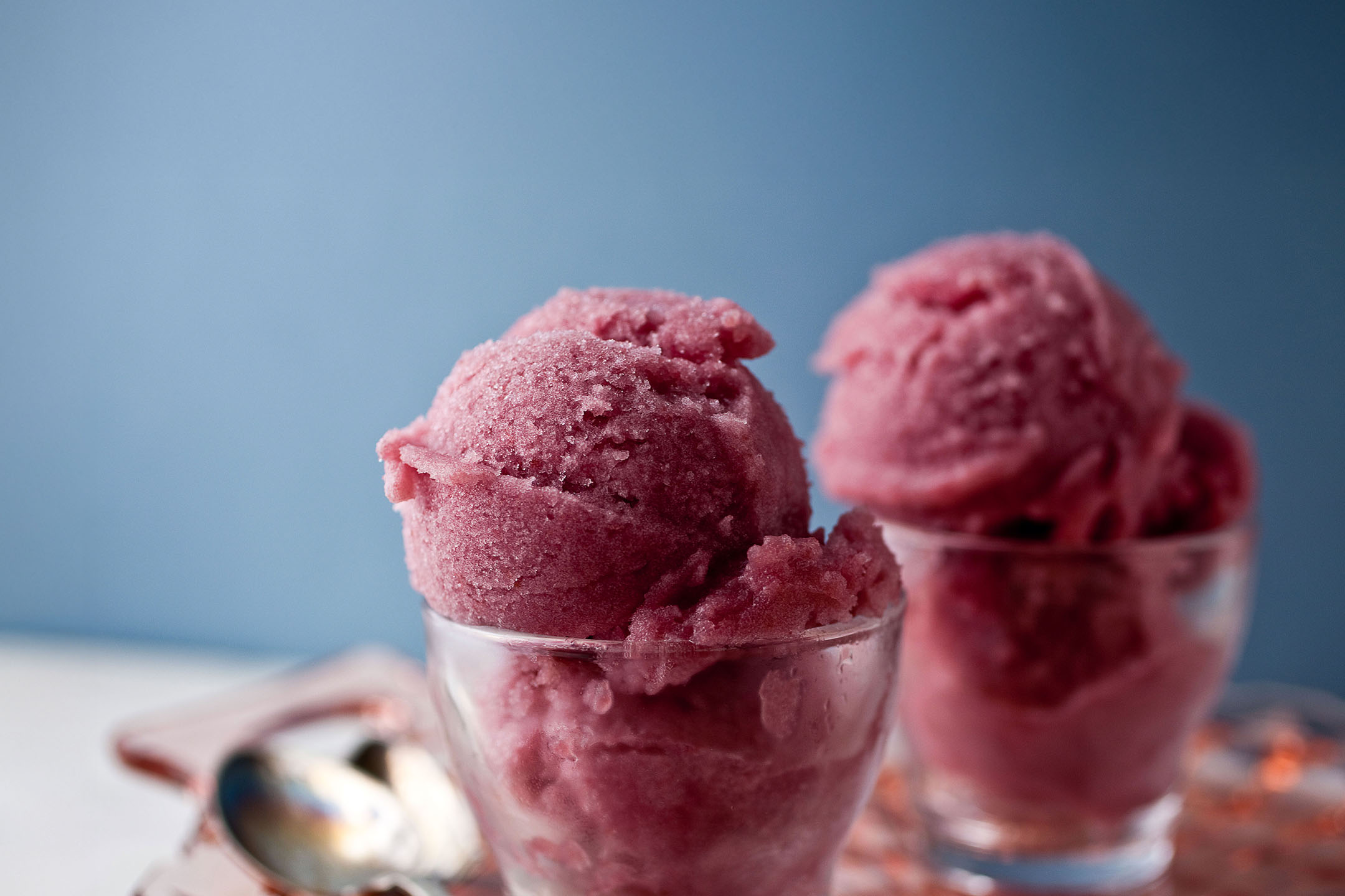 Zwei Gläser rosa Sorbet oder Eis auf einem weißen Tisch mit blauem Hintergrund.