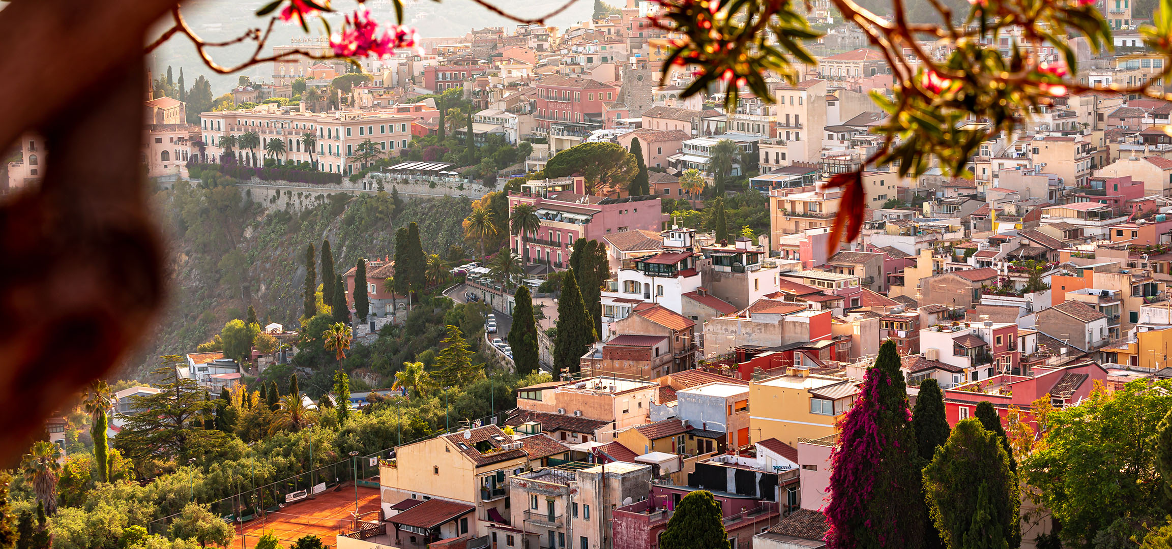 Panoramablick auf eine mediterrane Stadt mit farbenfrohen Gebäuden und Grünflächen.