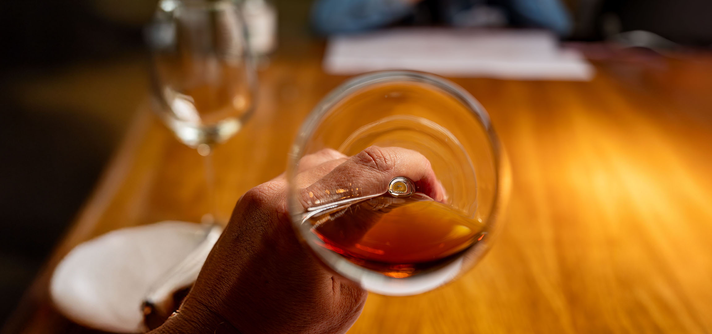 Nahaufnahme einer Hand, die ein Glas mit bernsteinfarbener Flüssigkeit, möglicherweise Whisky oder Brandy, hält.