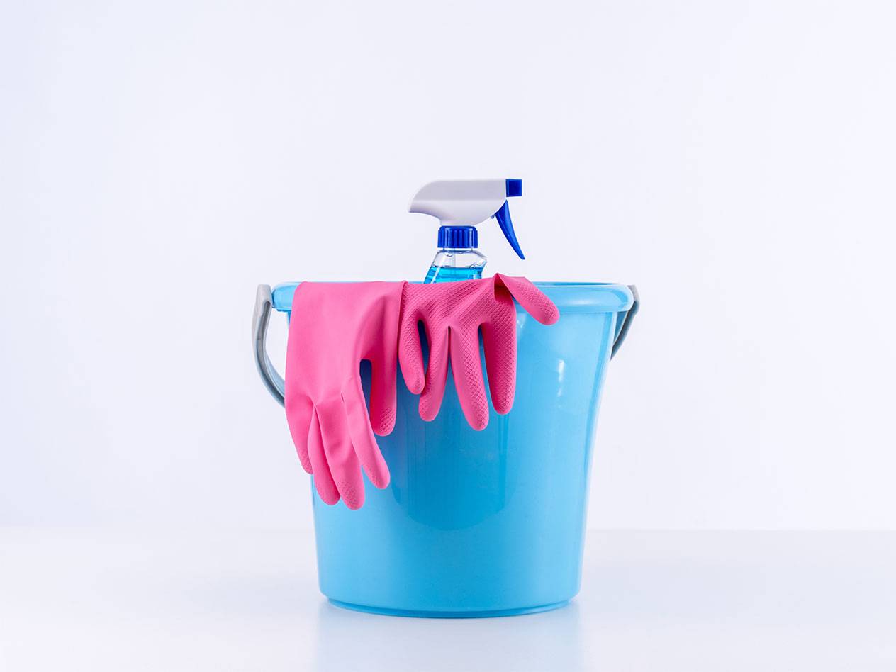Blauer Eimer mit pinken Putzhandschuhen und einer Sprühflasche.