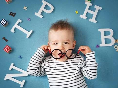 Baby mit Brille und Holzbuchstaben.