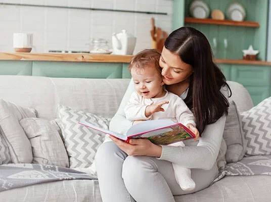 Eine Mutter liest ihrem Kind ein Buch auf dem Sofa vor.