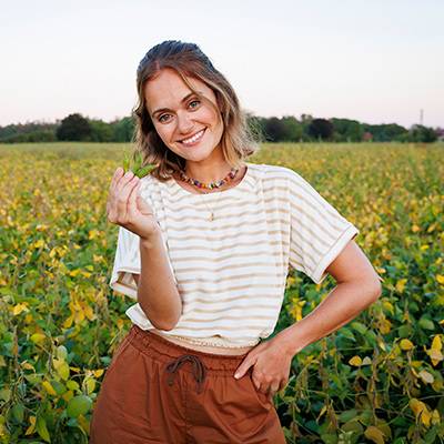 Frau auf einem Sojabohnenfeld, trägt ein gestreiftes Shirt und eine braune Hose.