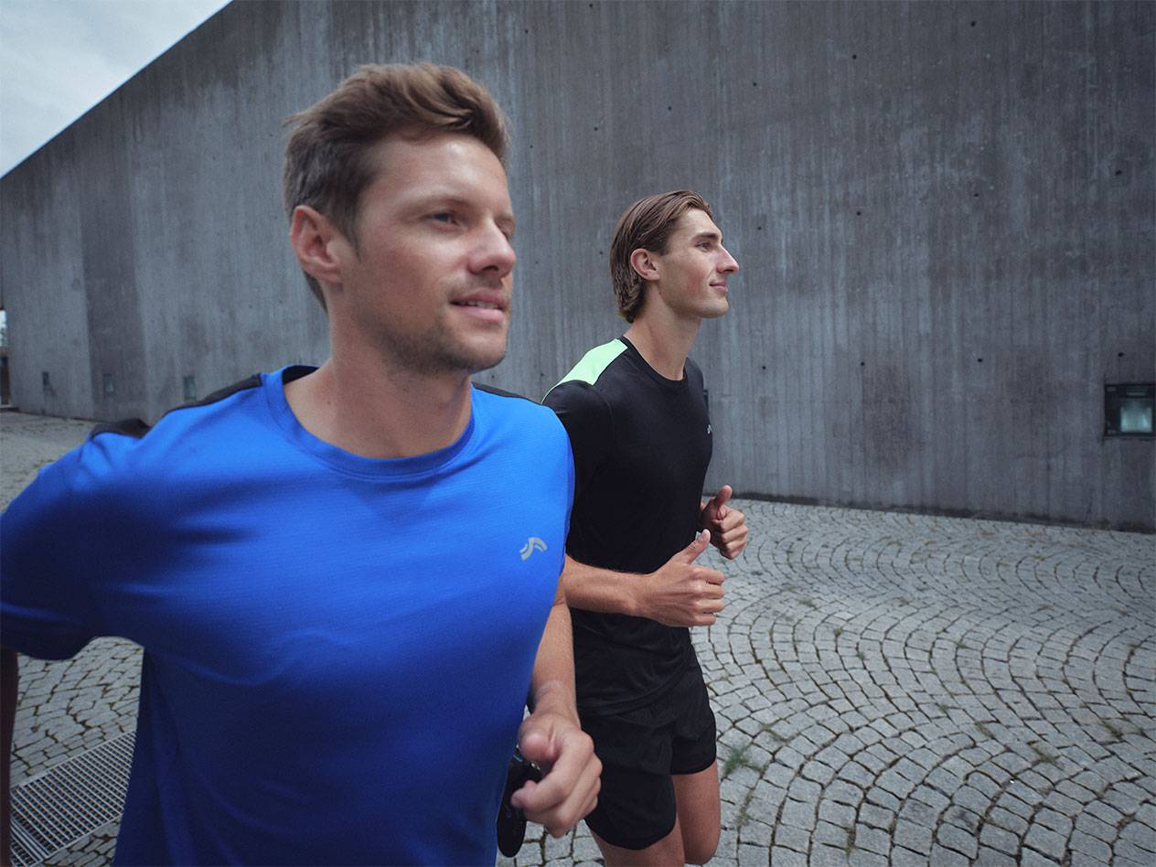 Zwei Männer laufen in Sport-T-Shirts und Shorts, eines blau und eines schwarz.