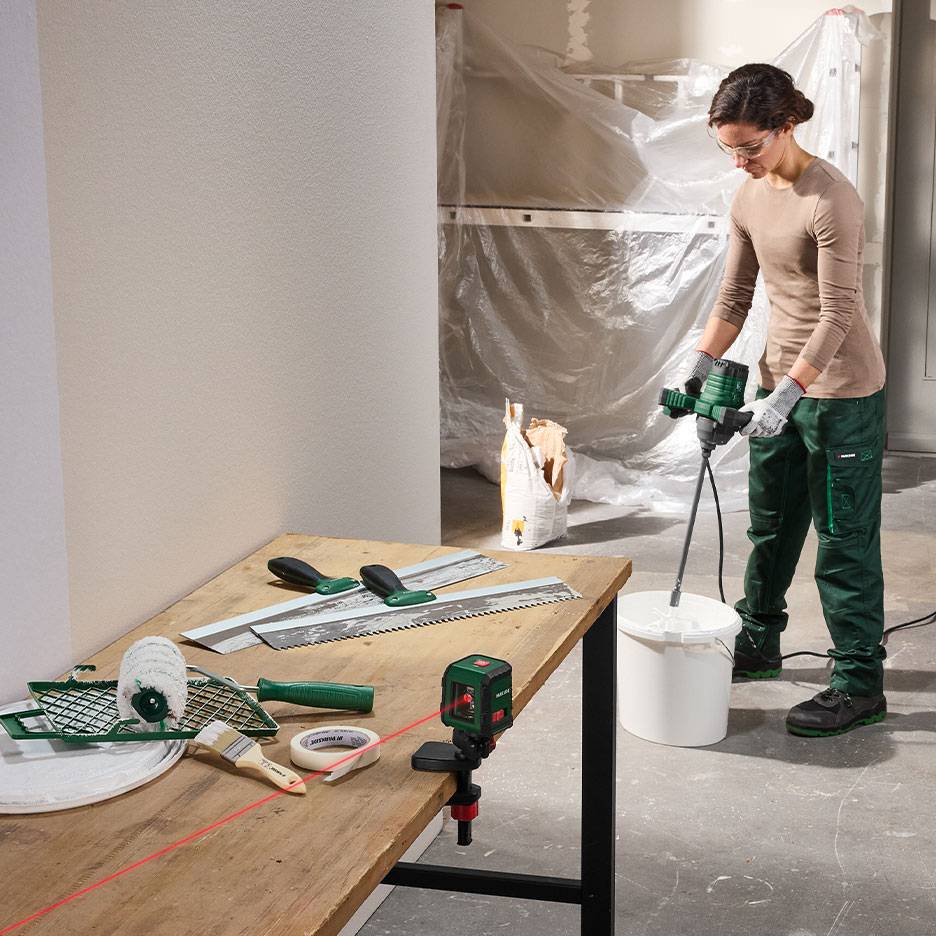 Frau mischt Baumaterial mit Maler- und Nivellierwerkzeugen auf einem Tisch.