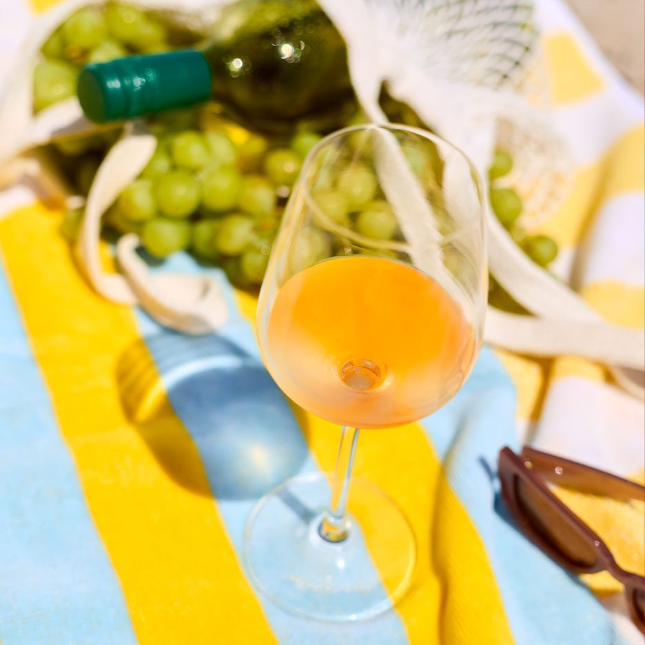 Glas Orangewein auf einem gestreiften Handtuch mit Trauben und einer Flasche im Hintergrund.