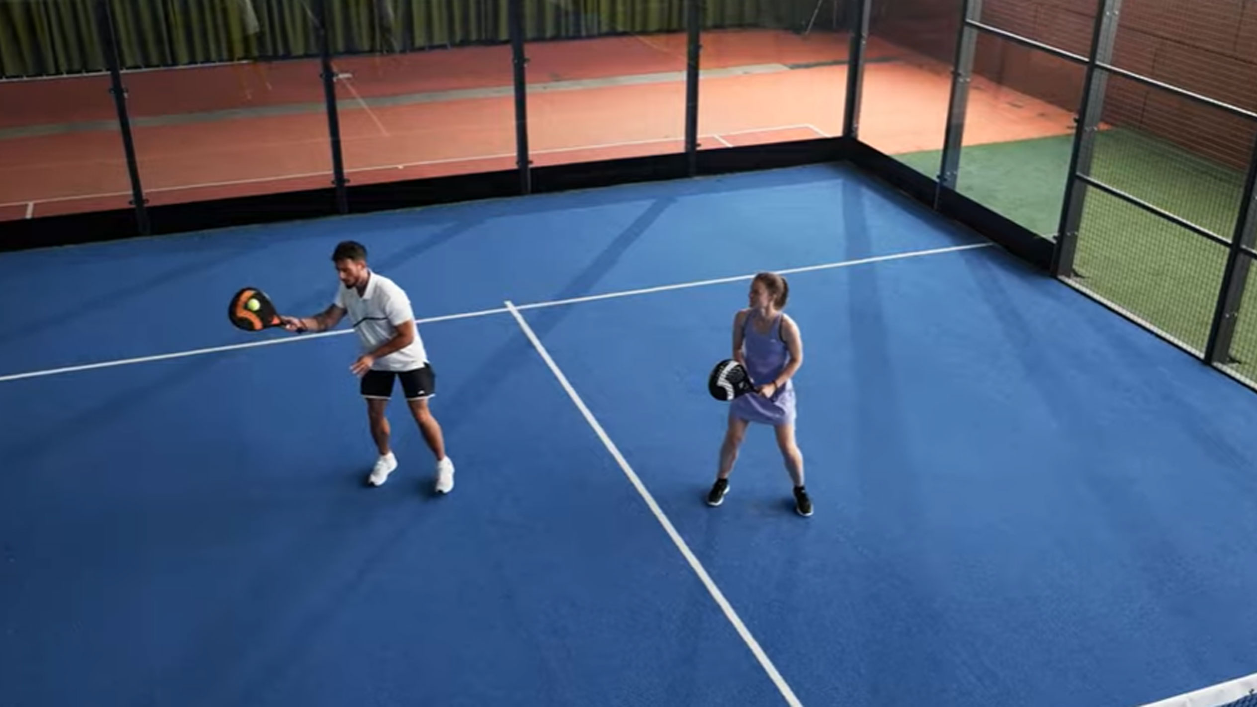 Mann und Frau spielen Padel auf blauem Platz mit Schlägern und Ball