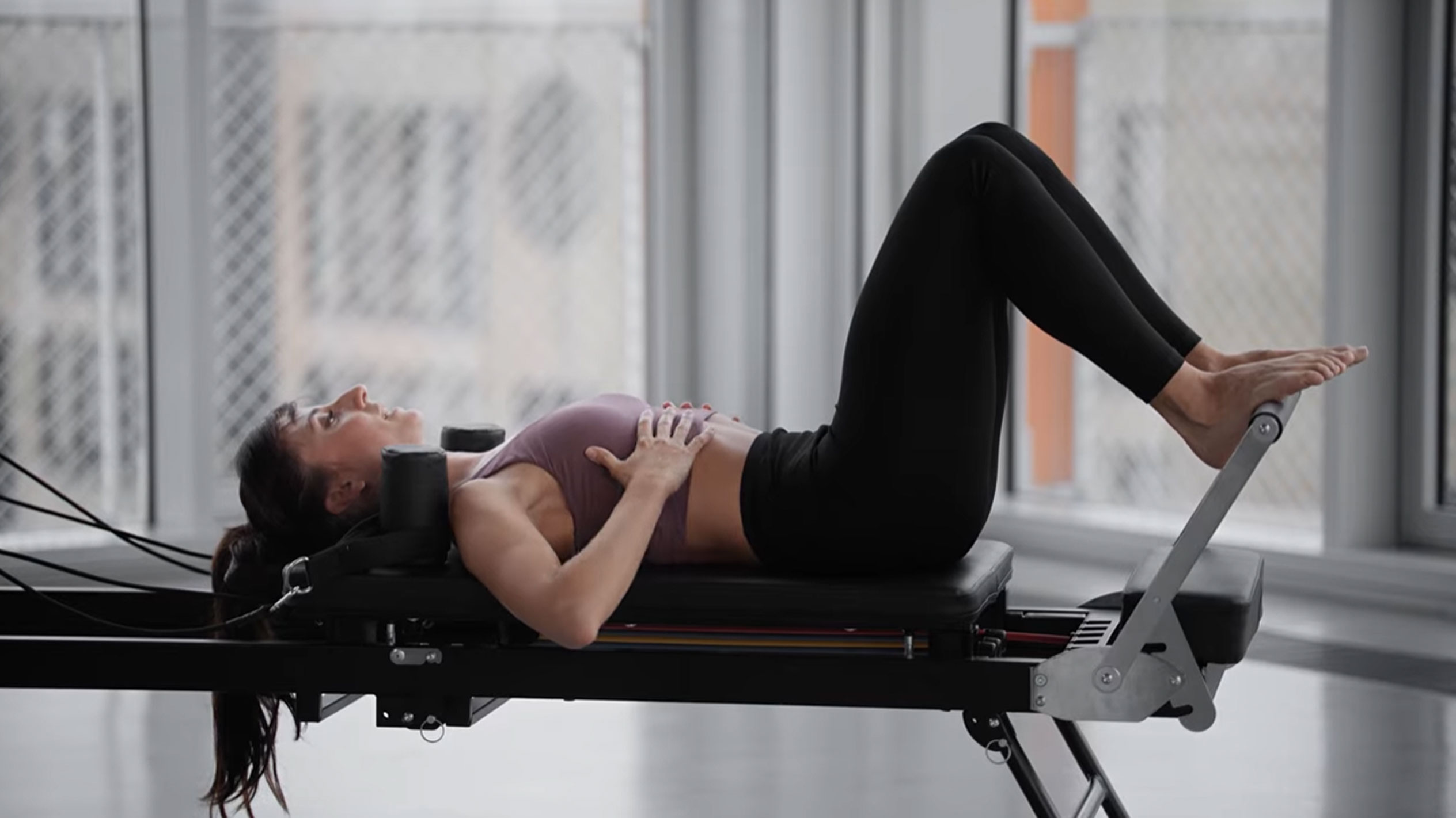 Frau macht Pilates auf einem Reformer, Hände auf der Brust.