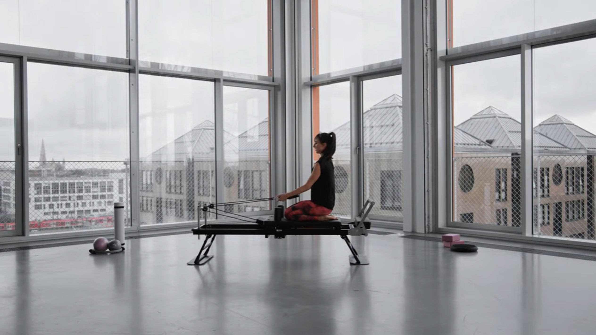 Frau macht Pilates auf einem Reformer, mit Blick auf die Stadt.