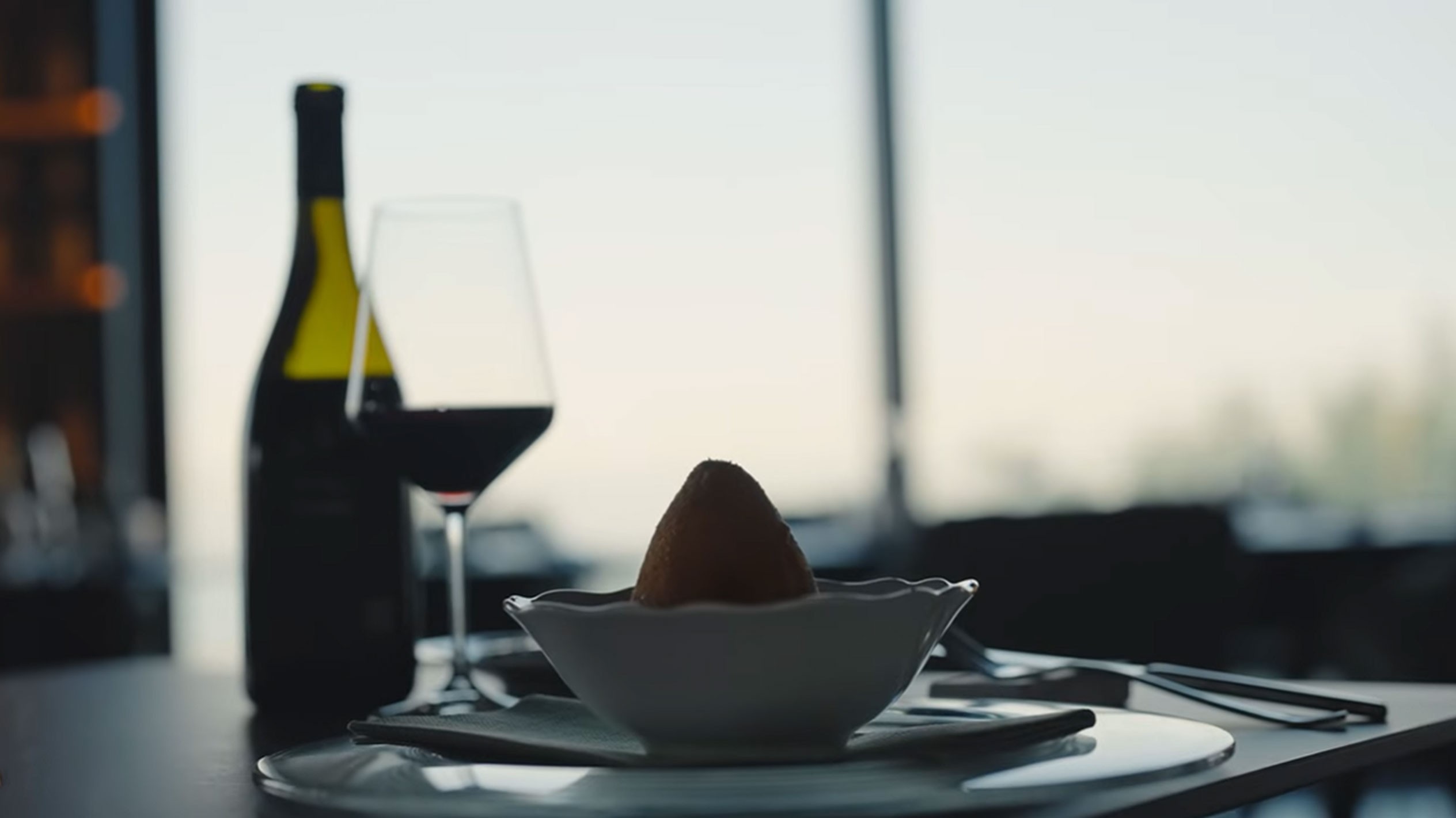 Eine Flasche Rotwein und ein Glas neben einem Arancino in einer Schale auf einem Tisch.