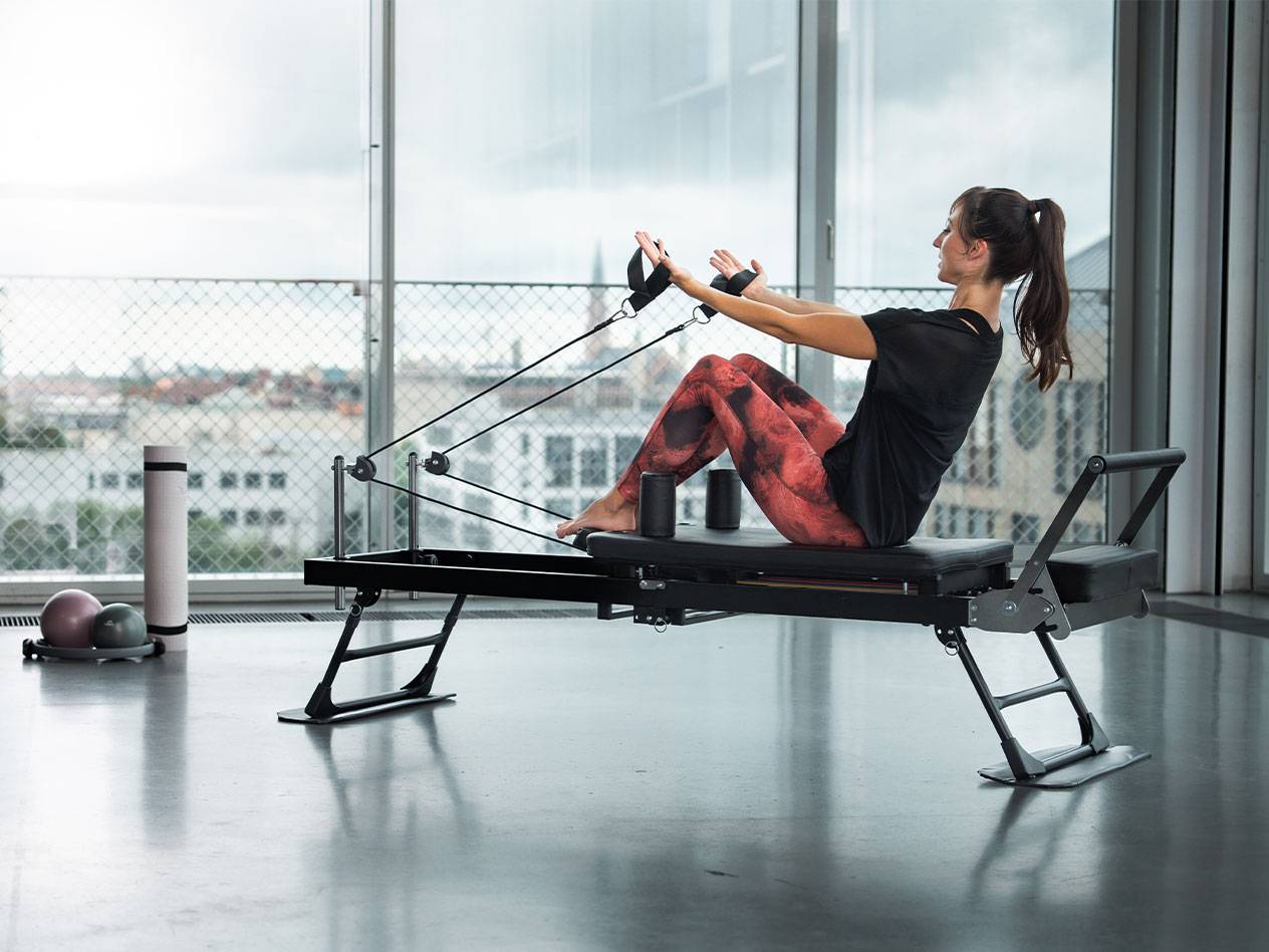 Frau macht Pilates auf einem Reformer mit Stadtblick.