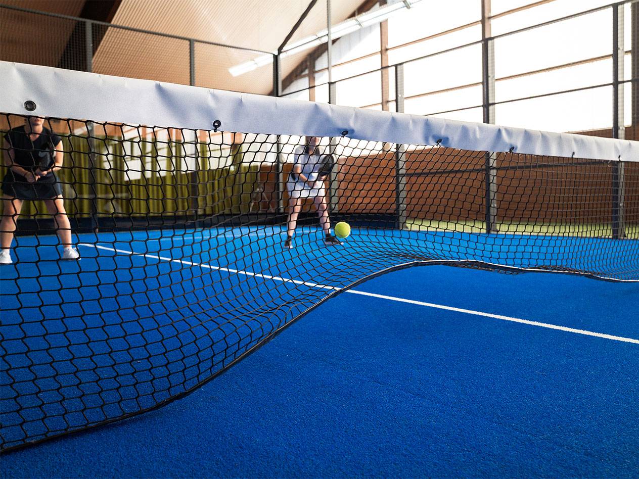 Zwei Frauen spielen Padel auf einem blauen Platz, mit dem Netz im Vordergrund.