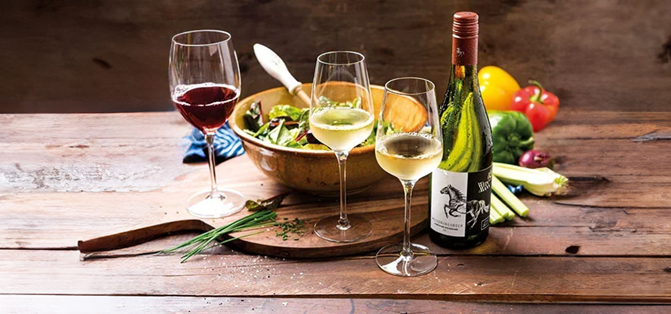 Wein, Salat und Gläser auf einem Holztisch.