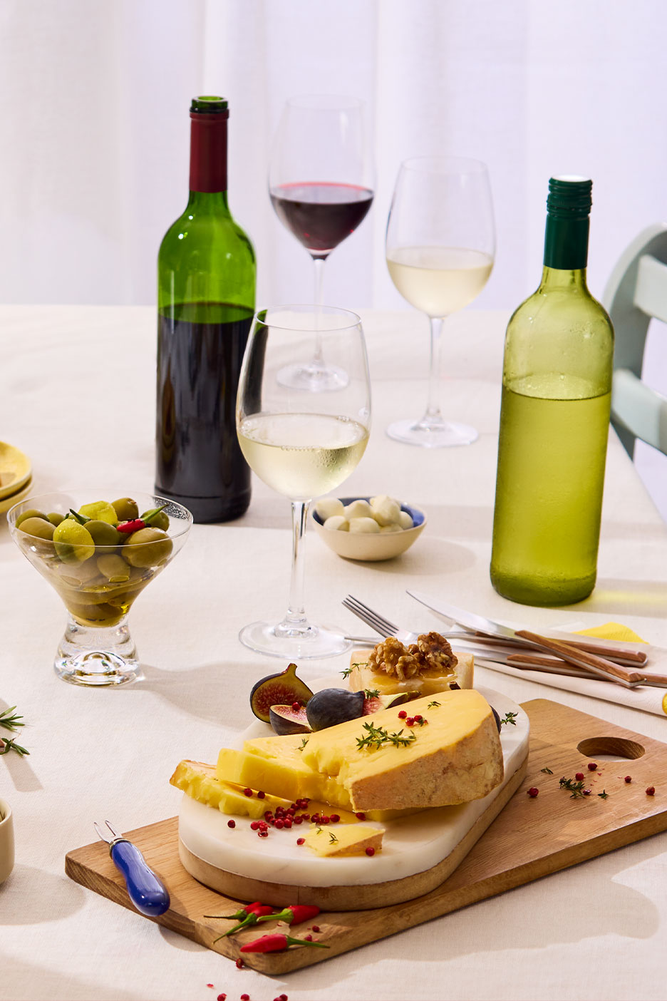 Flaschen und Gläser mit Rot- und Weißwein, Oliven, Käse und Feigen auf einem Tisch.