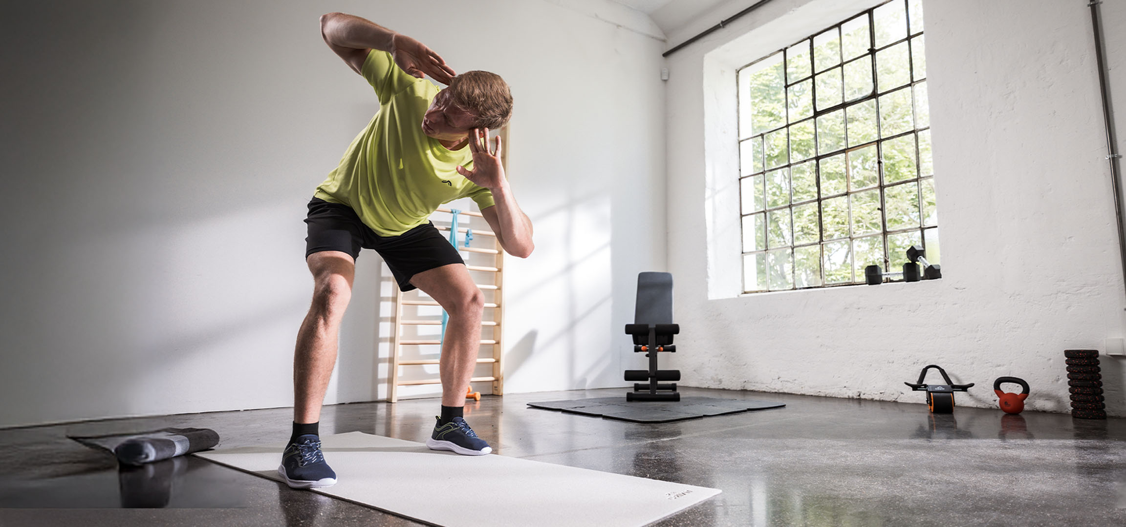 Mann trainiert im Fitnessstudio, nutzt Yogamatte und Hanteln.