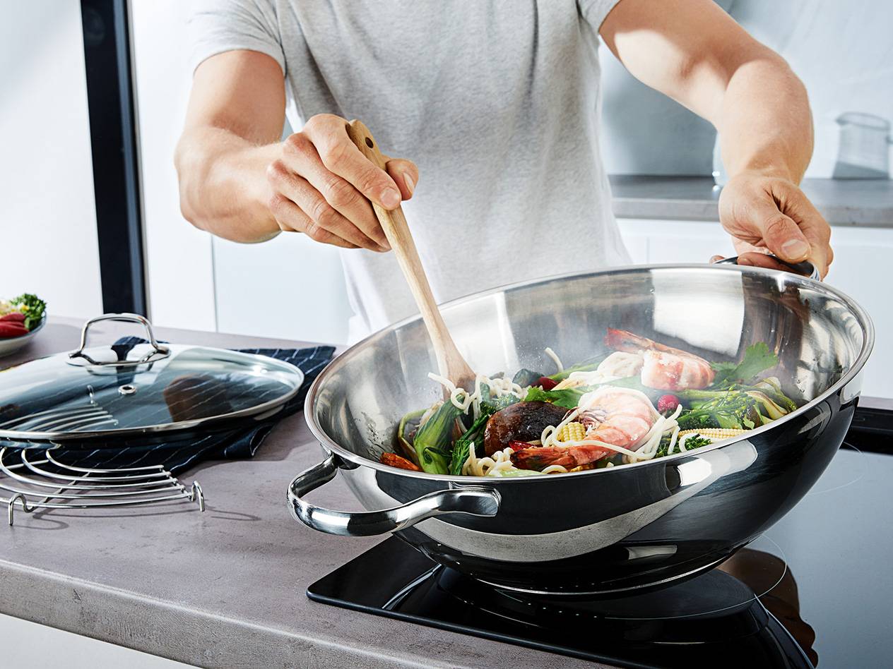 Essen in der Wokpfanne, Deckel und Dampfkorb daneben.