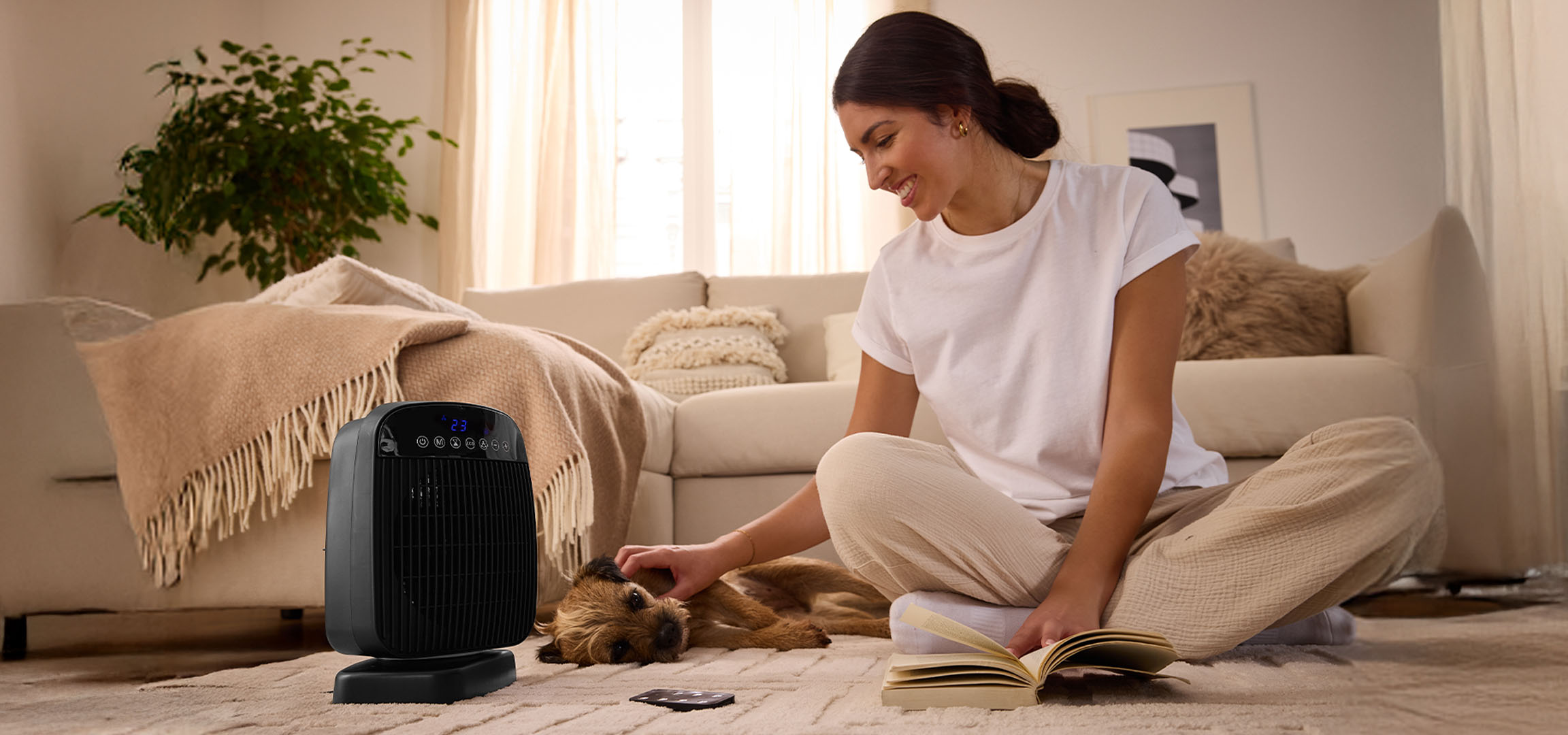 Eine Frau spielt mit einem Hund neben einem elektrischen Heizgerät im Wohnzimmer.