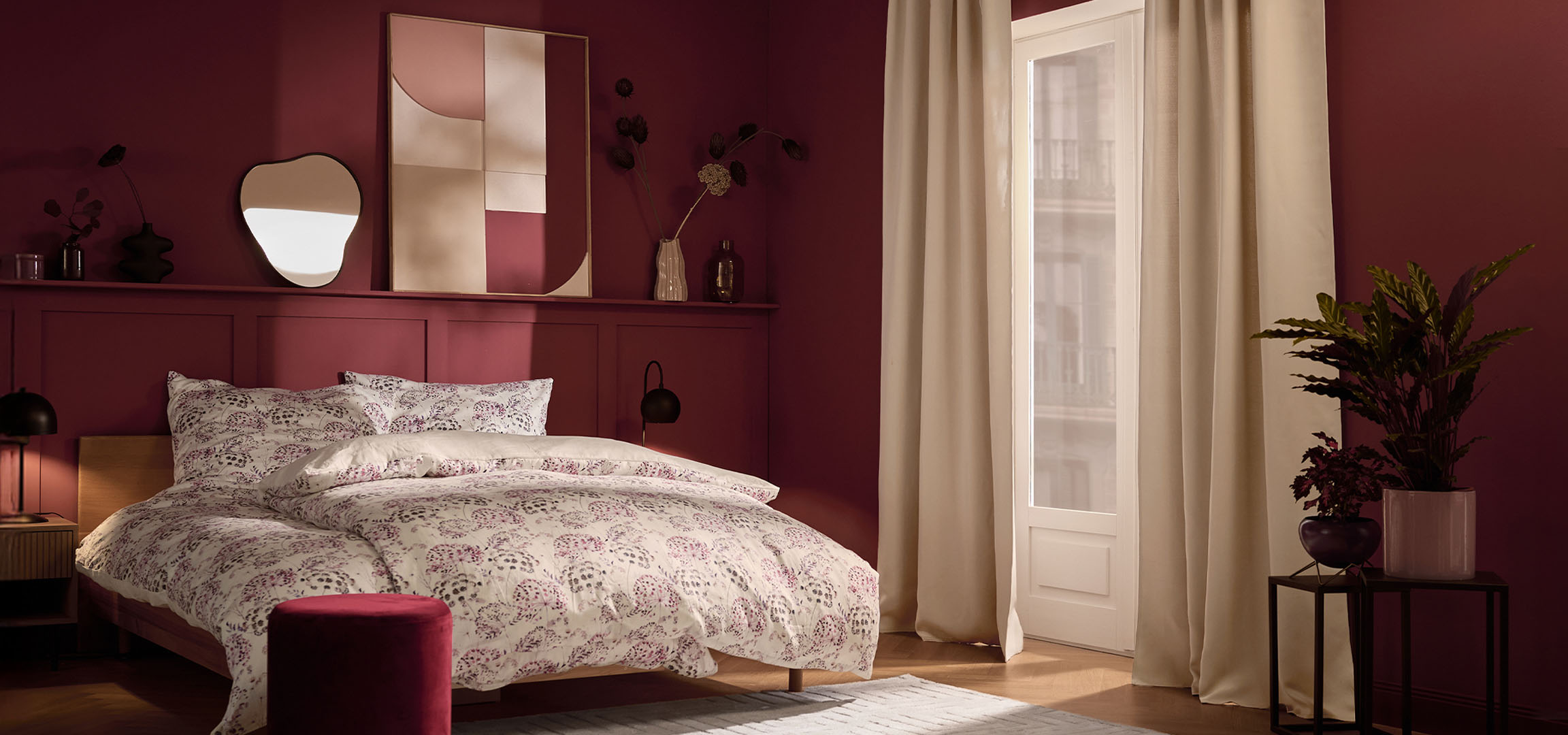 Schlafzimmer mit weinroten Wänden, Bett mit weißer Bettwäsche mit Blumenmuster und Pflanzen.