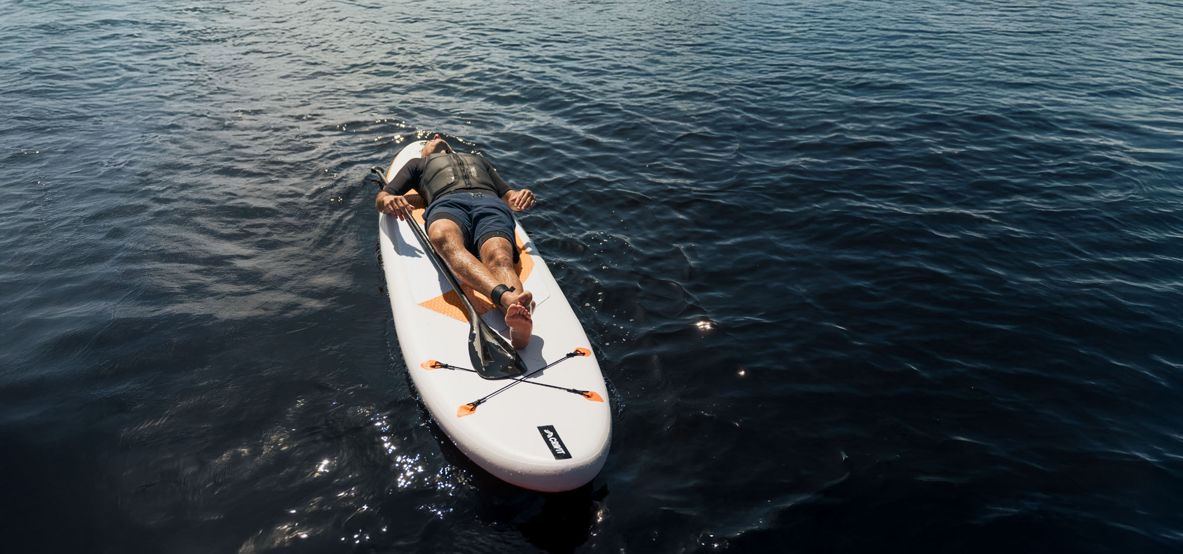 Mann entspannt sich auf einem Stand-Up Paddleboard im ruhigen Wasser.