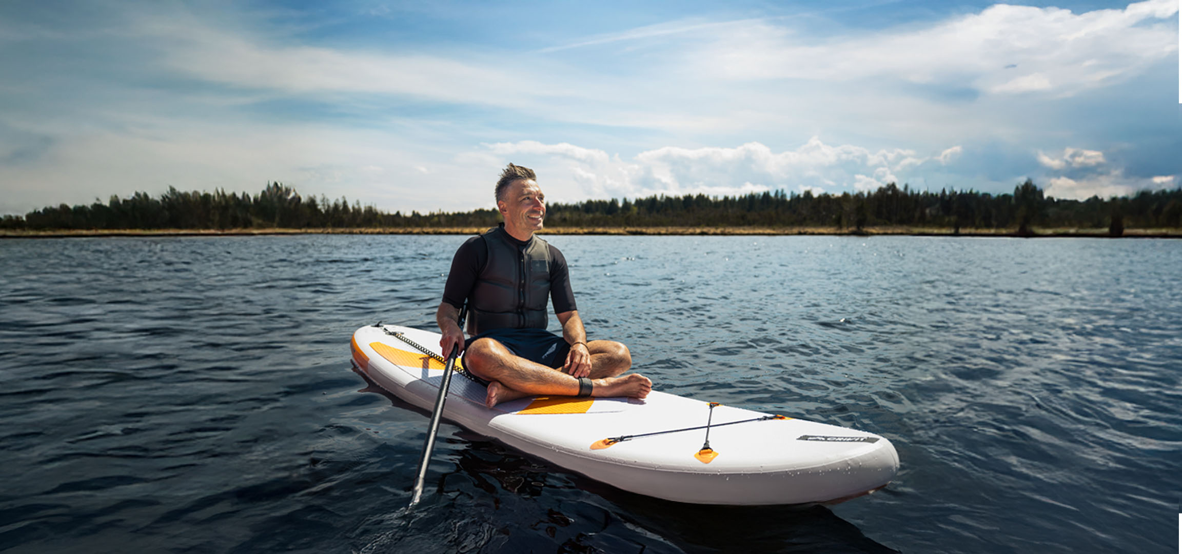 Mann paddelt auf einem See auf einem Stand-Up-Paddleboard.