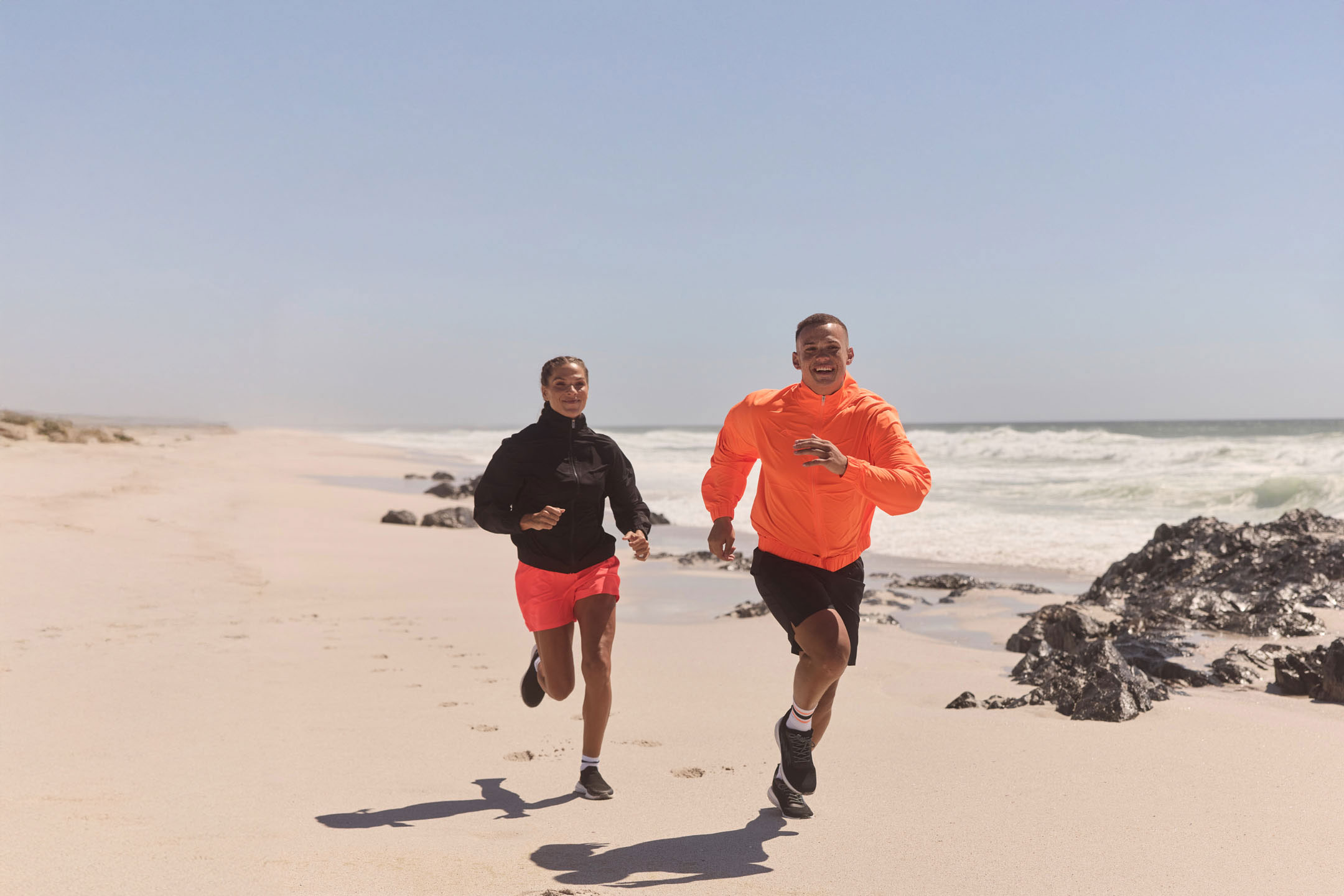 Zwei Personen joggen am Strand.