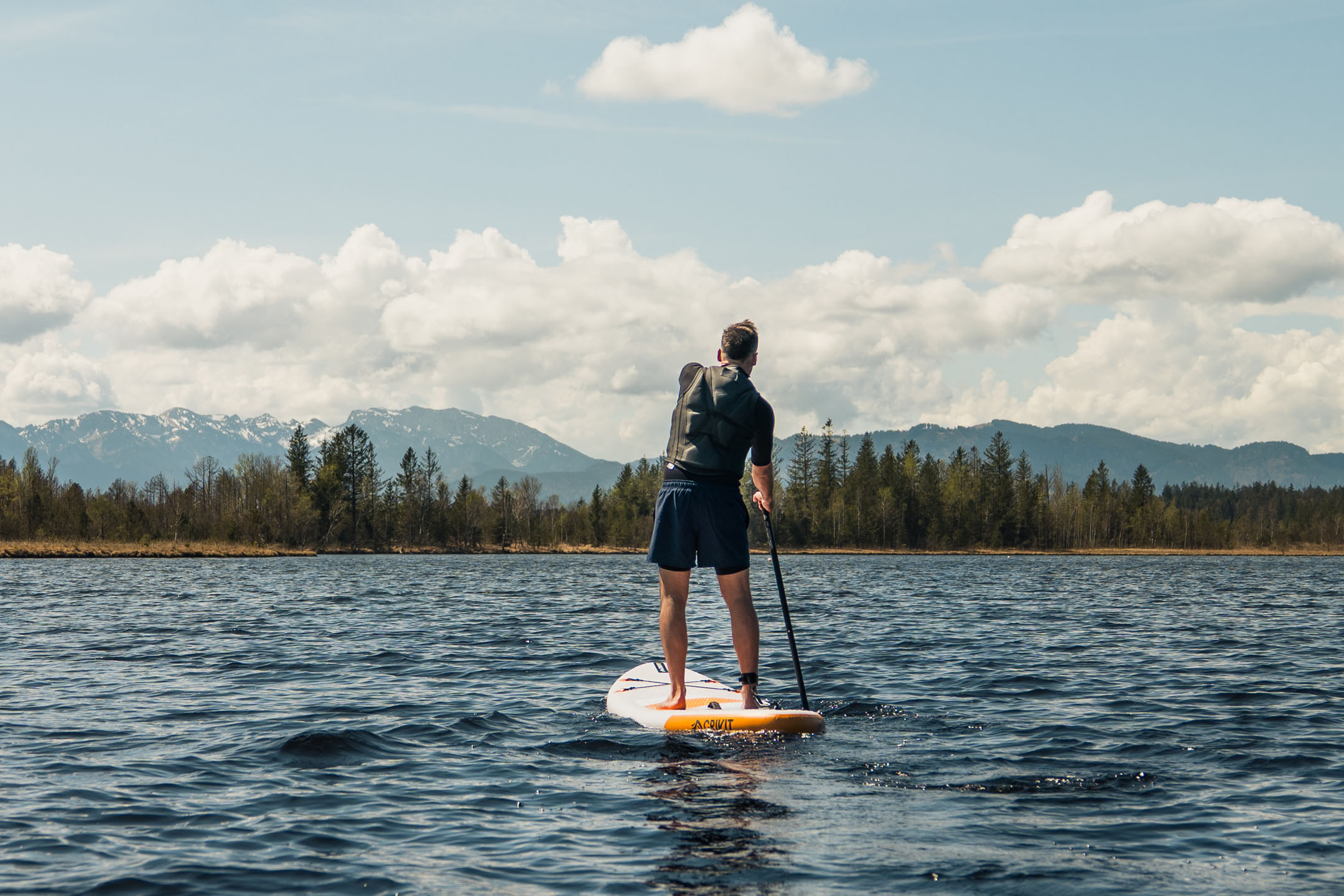 Stand-up-Paddleboarding auf einem See mit Bergen im Hintergrund.