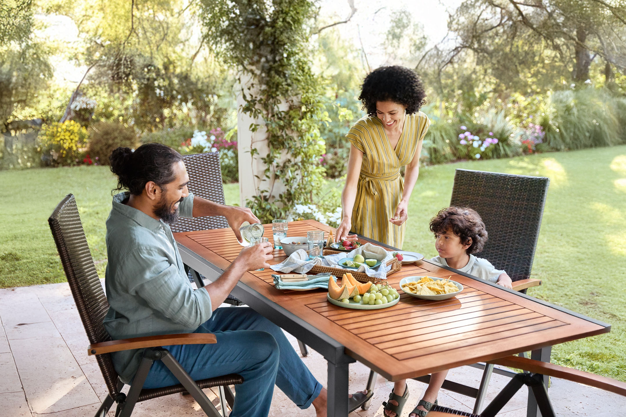 Familienessen im Freien mit Holztisch und Rattanstühlen.
