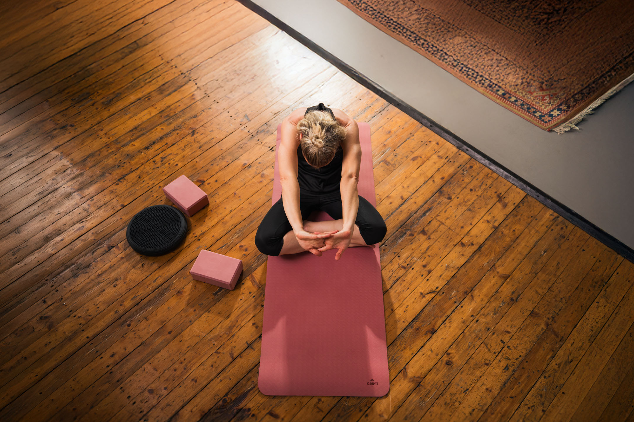 Frau macht Yoga auf einer rosa Matte mit Blöcken und Balancekissen.