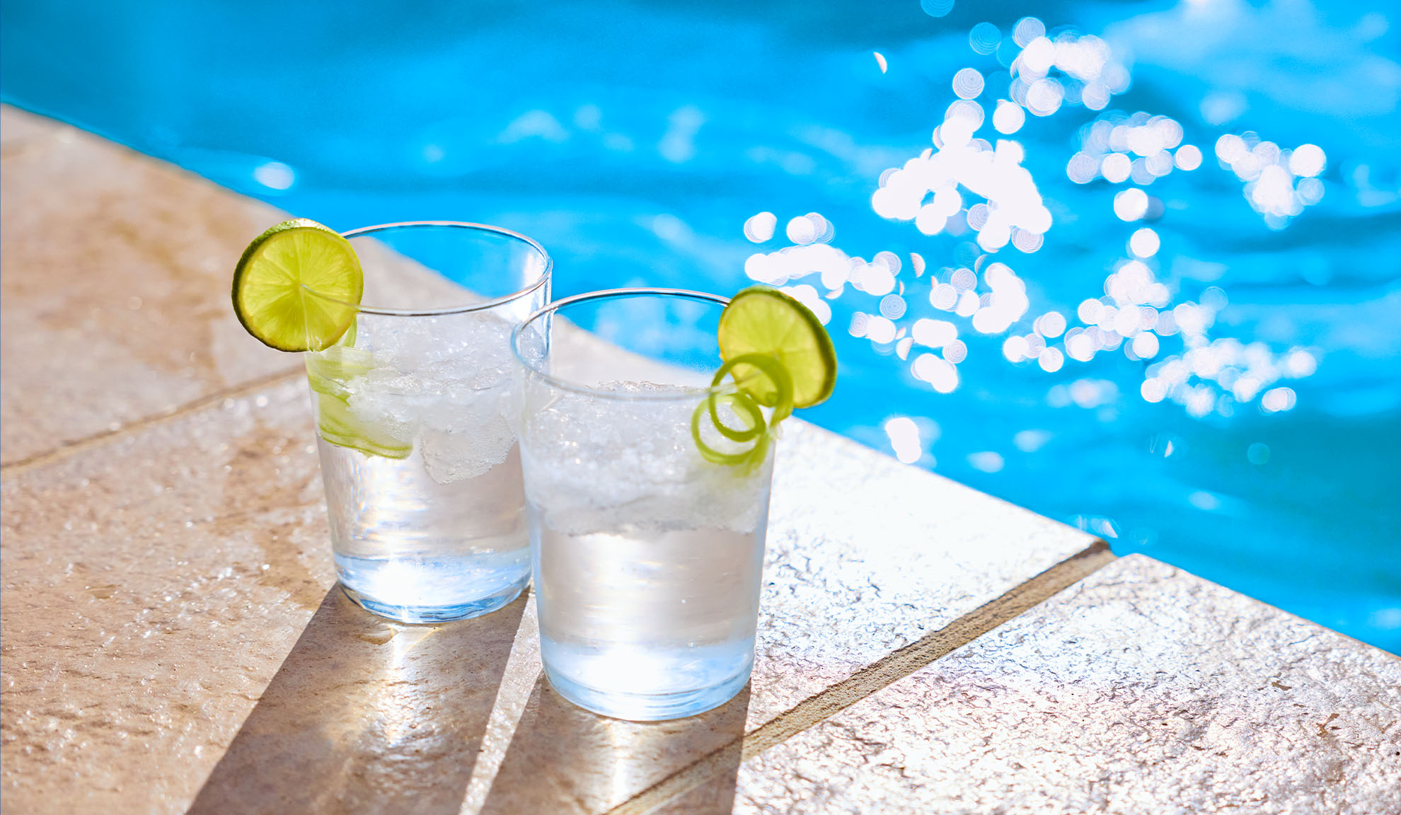 Zwei erfrischende Getränke mit Limette an einem funkelnden blauen Pool.
