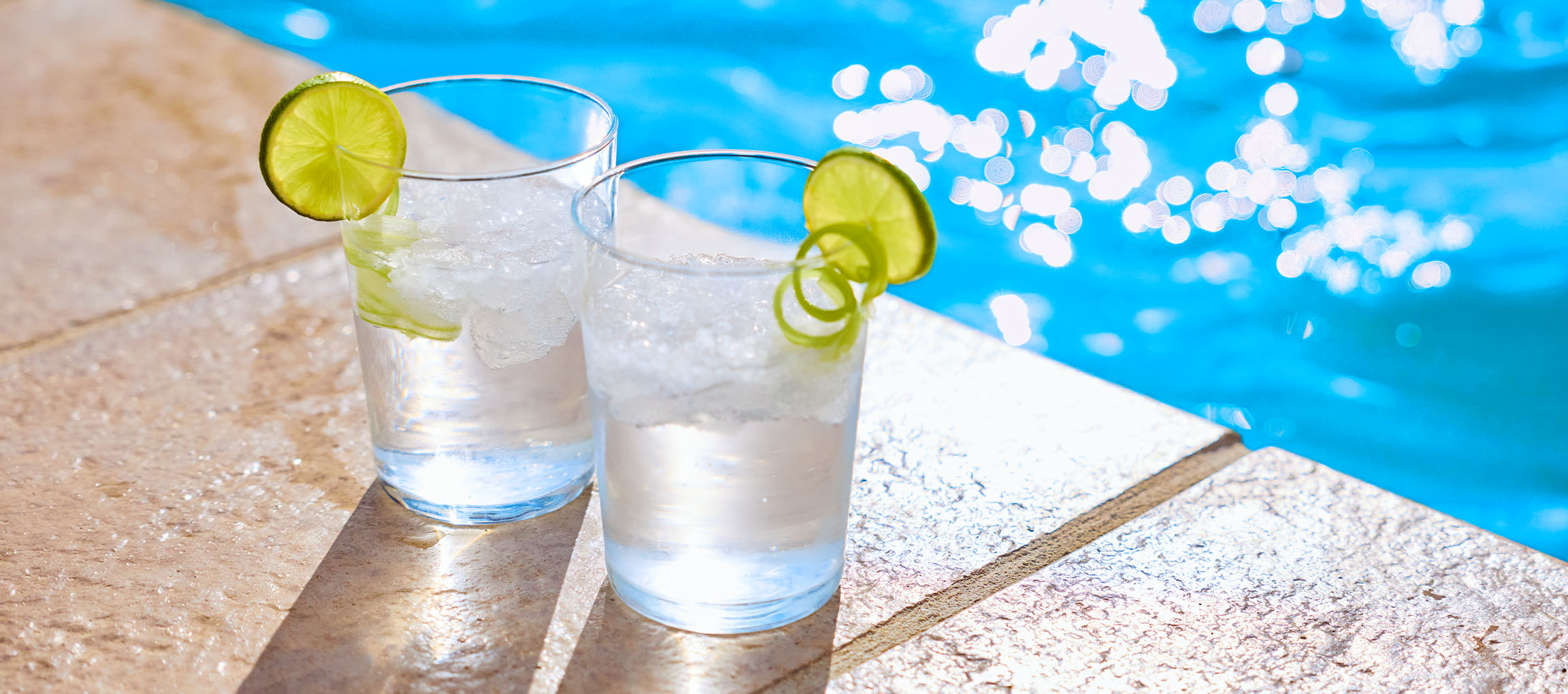 Zwei Gläser Erfrischungsgetränk mit Limetten am Pool.