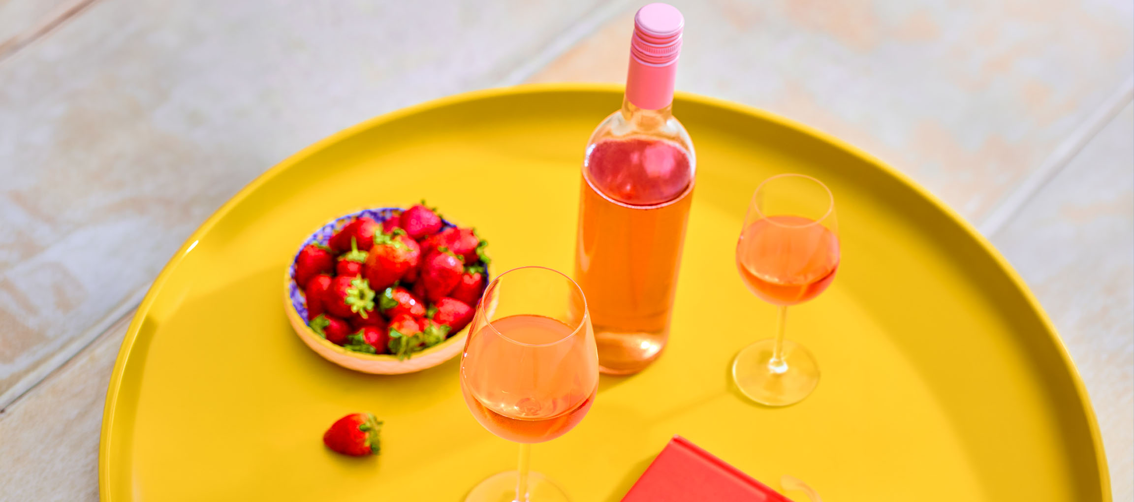 Roséwein in Flasche und Gläsern mit Erdbeeren auf gelbem Tablett