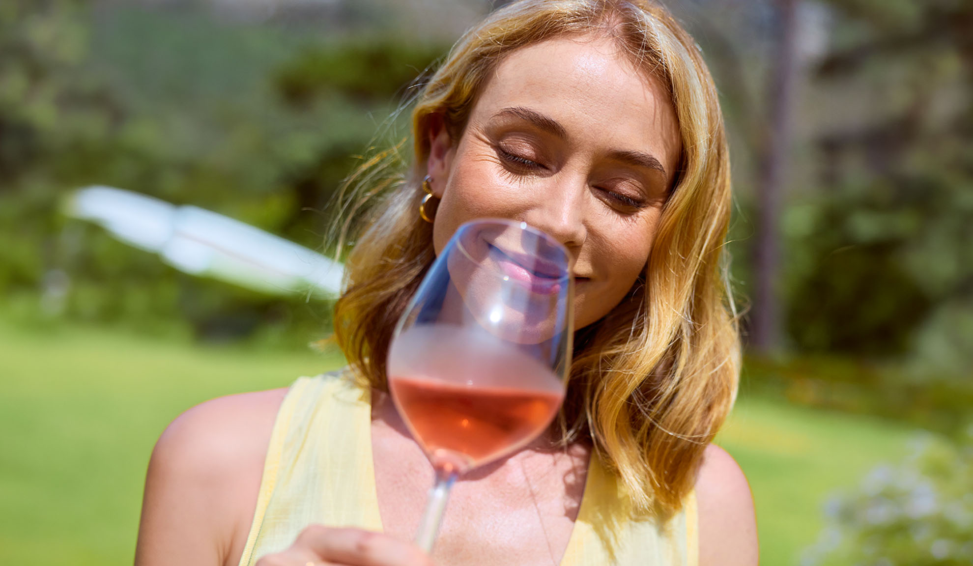 Lächelnde Frau riecht an einem Glas Roséwein im Freien.