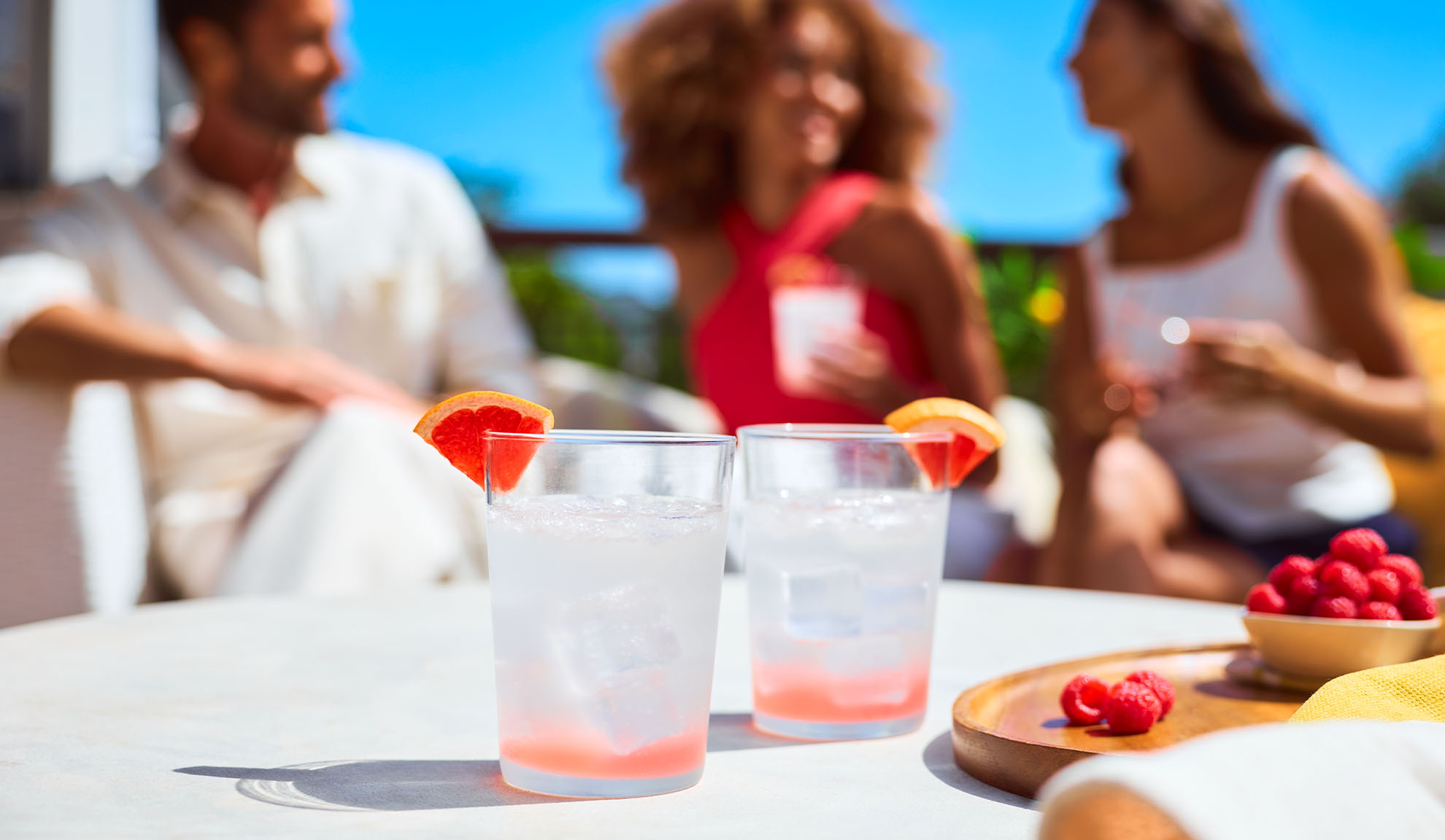 Zwei erfrischende Grapefruitgetränke mit Himbeeren auf einer sonnigen Terrasse mit Freunden.