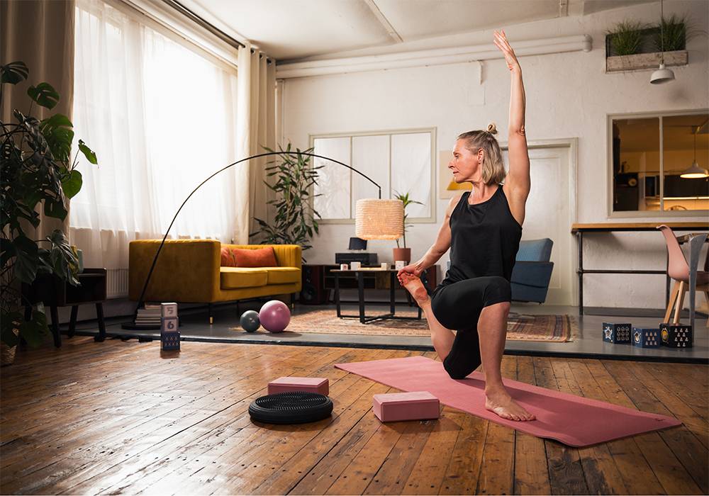 Frau macht Yoga zu Hause mit Matte, Blöcken und Balance-Disc.