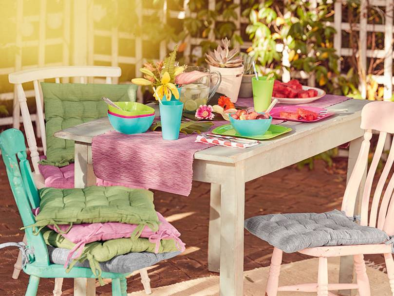 Gartenmöbelkissen, buntes Geschirr und Tisch.