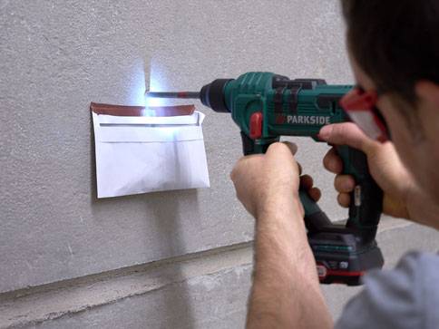Ein Mann bohrt mit einem Parkside Bohrer ein Loch in die Wand für einen Briefumschlag.