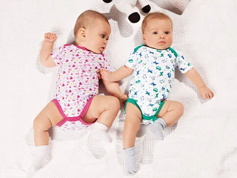 Zwei Babys in Bodys mit Herz- und Flugzeugmotiven.