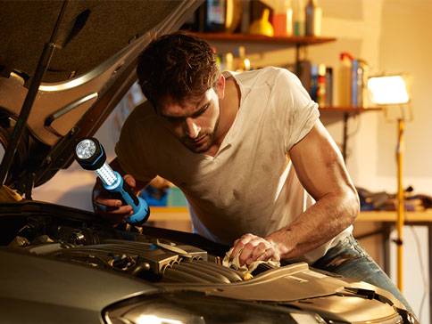 Mann repariert Auto mit LED-Taschenlampe.