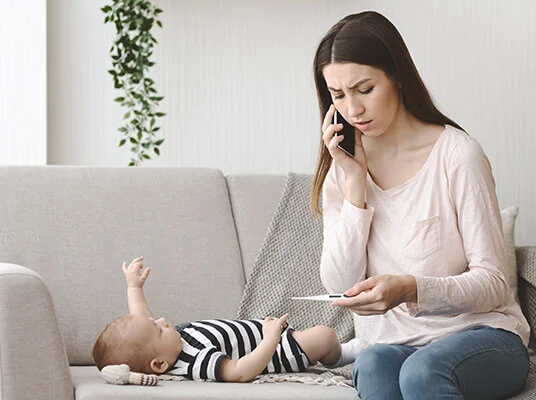Mutter telefoniert und misst die Temperatur ihres Babys.