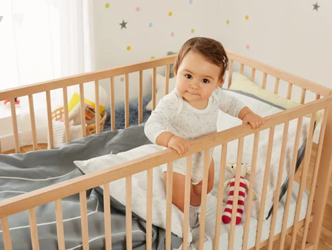 Baby in Holzbett, Decken und Spielzeug.