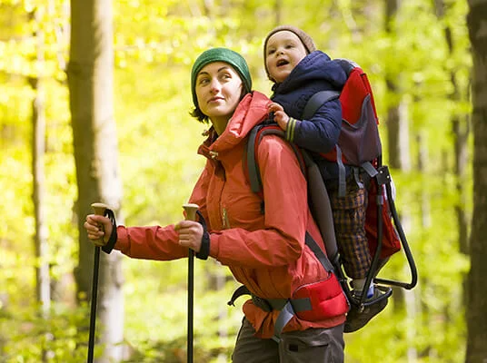 Wanderung im Wald: Mutter mit Kind im Tragegestell und Wanderstöcken.