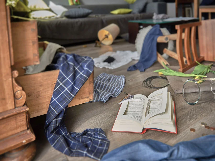 Unordentliches Zimmer mit Buch, Kleidung und antikem Schrank.