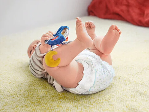 Baby spielt mit Rassel und trägt Windel.