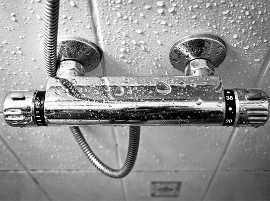 Duschkopf und Thermostatarmatur in feuchtem Badezimmer.