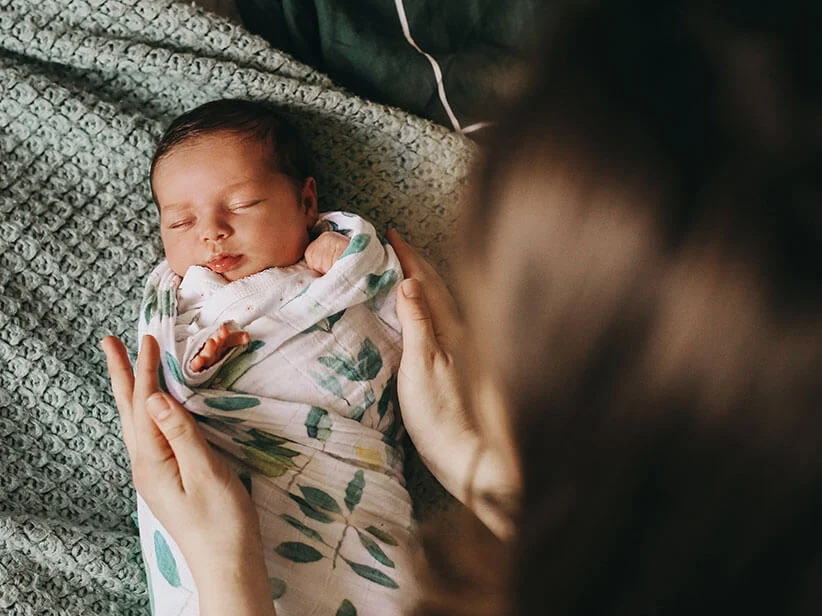 Neugeborenes Baby in weicher Decke mit Blattmotiv.