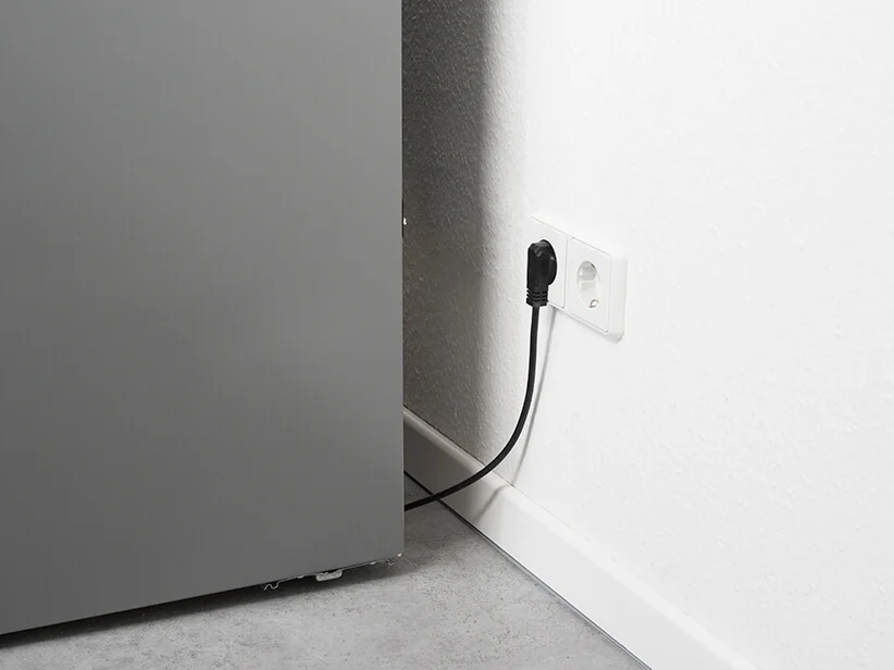 Grauer Kühlschrank an der Steckdose angeschlossen.