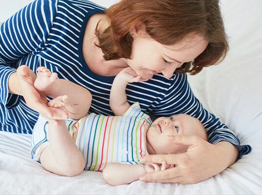 Mutter und Baby, Baby trägt einen Regenbogen-gestreiften Strampler.