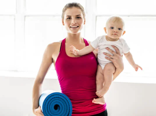 Eine Mutter hält ein Baby und eine Yogamatte.