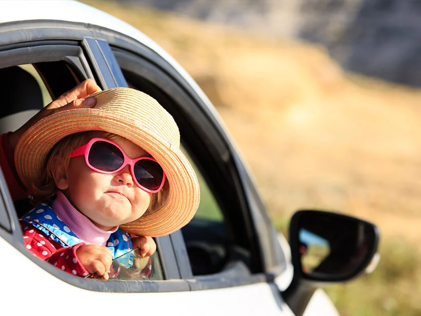 Baby im Auto mit Sonnenbrille und Strohhut.