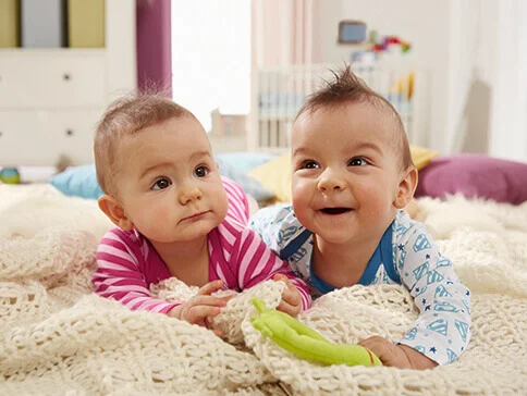 Zwei Babys auf einer Decke, eines in rosa, das andere in blau-weiß.